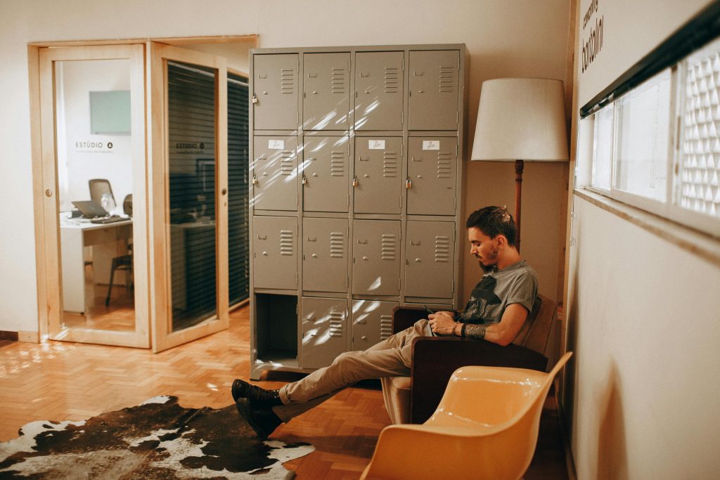 A relaxed man sits in a contemporary office, featuring lockers and stylish furniture, creating a cozy workspace.
